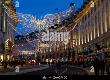 Weihnachtsbeleuchtung der Engel über die Regent Street, London, mit busy holiday Shopper, am Abend. Stockfoto