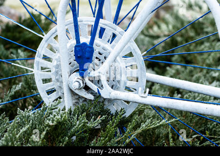 Teile von einem Fahrrad stehen im Garten wie Dekorationen, lackiert in Blau und Weiß Stockfoto