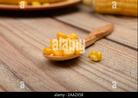 Körner von Mais auf einem Löffel aus Holz, auf einem Holztisch, im Hintergrund gekochten Mais und unbehandelten Ähren. Fitness Ernährung. Gesunde Ernährung. Für eine Stockfoto