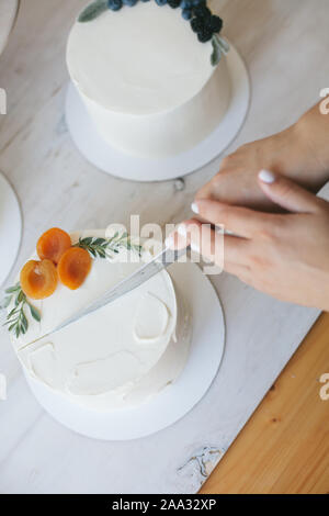 Frau schneiden einen Kuchen mit buttercream Vereisung und Pfirsiche Stockfoto