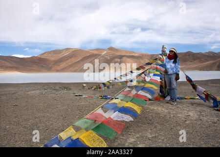 Reisende thaifrau Reisen besuchen Sie stand für ein Foto mit Gebetsfahnen für Segen am Aussichtspunkt mit Bergen und Pangong See während der Wintersaison Stockfoto