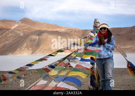 Reisende thaifrau Reisen besuchen Sie stand für ein Foto mit Gebetsfahnen für Segen am Aussichtspunkt mit Bergen und Pangong See während der Wintersaison Stockfoto