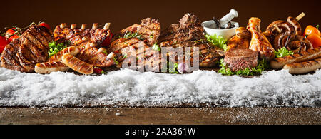 Layout der frisch gegrilltes Fleisch Produkte zeigte auf Holztisch mit Schnee im winter Thema Banner gegen braunen Hintergrund Stockfoto