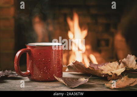 Rot Tasse mit heißem Tee vor einem brennenden Kamin, Komfort und Wärme des Herdes Konzept. Stockfoto