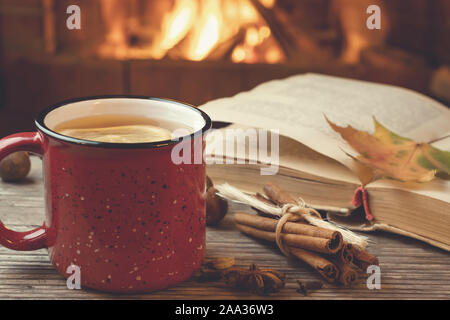 Rot Tasse mit heißem Tee und ein offenes Buch vor einem brennenden Kamin, Komfort, Entspannung und Wärme des Herdes Konzept. Stockfoto