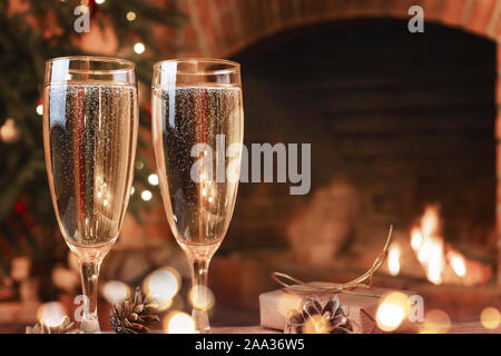 Zwei Gläser mit Champagner auf einer hölzernen Tisch in einem Raum mit einer brennenden Kamin. Stockfoto