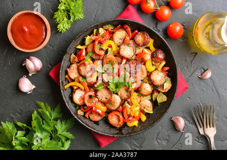 Scheiben von gebratenem Gemüse mit Würstchen und Gewürzen in der Pfanne. Ansicht von oben, flach Stockfoto