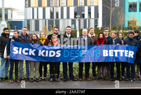 Edinburgh, Schottland, Großbritannien. 19. November 2019. Der Schottischen Konservativen banner enthüllen außerhalb der neuen unfertig und viel-königlichen Krankenhaus für Kinder und Jugendliche in Edinburgh verzögert. Shadow Gesundheit Sekretärin Meilen Briggs, von Jackson Carlaw MSP begleitet, vorgestellte Banner hervorgeht, wie der Nationalisten (SNP) im Stich gelassen haben die jungen Patienten und ihre Familien nicht nur in Edinburgh, aber über dem Land. 19. November 2019. Iain Masterton/Alamy Leben Nachrichten. Credit: Iain Masterton/Alamy leben Nachrichten Stockfoto