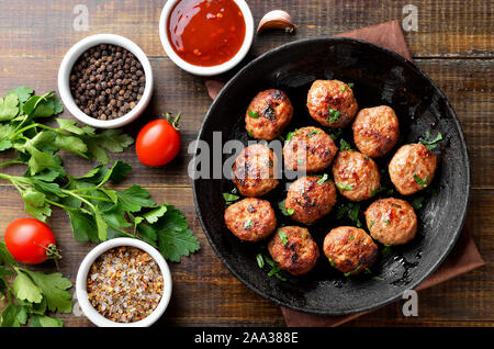 Gebratene Koteletts aus Hackfleisch/Faschiertem in der Pfanne und Gewürzen auf Holztisch. Ansicht von oben, flach Stockfoto