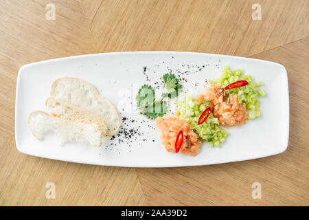 Lachstatar mit Gurke und Sesam. Verkostung Teller auf einen hölzernen Tisch. Stockfoto