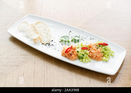 Lachstatar mit Gurke und Sesam. Verkostung Teller auf einen hölzernen Tisch. Stockfoto