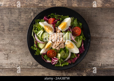 Salat mit Thunfisch, Ei und Gemüse auf schwarze Platte und Holztisch. Ansicht von oben. Stockfoto