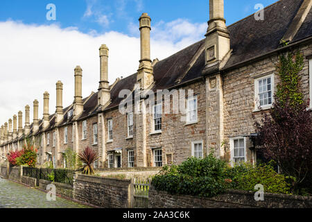 Zeile des 14.jahrhunderts Reihenhäuser mit hohen Kaminen und kleinen Vorgärten auf gepflasterten Straße in die vikare Schließen, Brunnen, Mendip, Somerset, England, Großbritannien Stockfoto