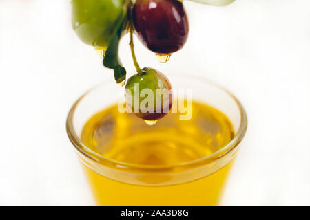 Kleine Glasschale mit Olivenöl, mit einem kleinen Zweig mit Oliven, Obst, auf weißem Hintergrund eingerichtet Stockfoto