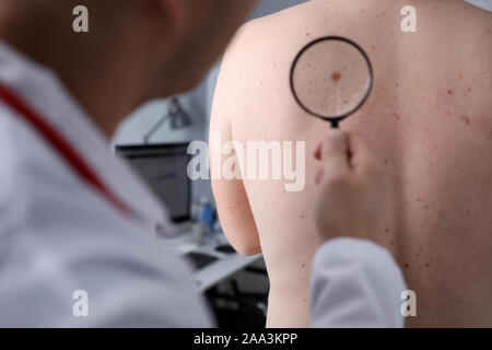 Männlicher Arzt Blick auf die Lupe auf der Haut des Patienten Stockfoto