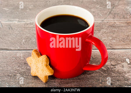 Rot Tasse mit schwarzem Kaffee und Weihnachten Sterne Cookie auf rustikalen, verwitterte dunkelbraunen Hintergrund der Kontrollleiste gefüllt. Stockfoto