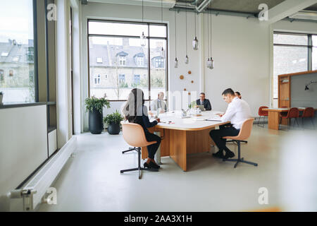 Gruppe von verschiedenen Unternehmern reden während der Sitzung um einen Konferenztisch in einem Büro Stockfoto