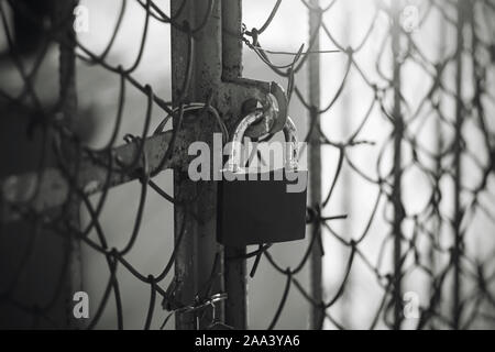 Ein schwarz-weißes Bild eines alten schäbigen Lock hängend an einem Metallgitter Tor, durch Licht beleuchtet. Stockfoto