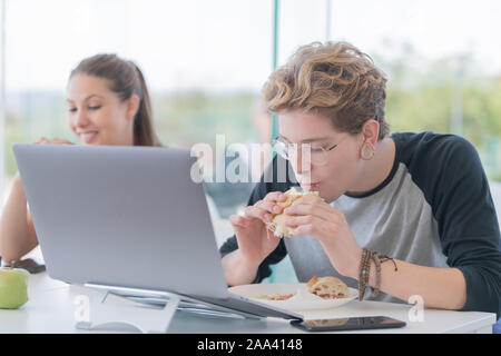 Junger Mann, ist das Essen ein Sandwich vor einem Computer. Konzept der Arbeit essen. Stockfoto