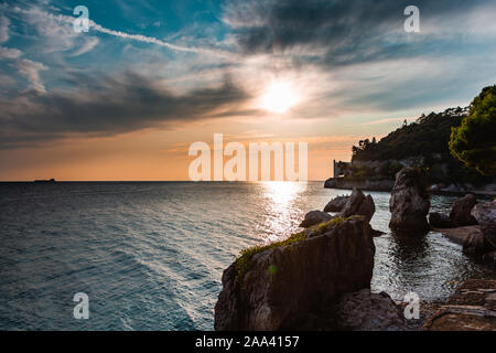 Dramatische Sicht auf das Mittelmeer Küste von Triest in Italien beim Sonnenuntergang, mit dem Schloss Miramare (Castello di Miramare) im Hintergrund. Stockfoto