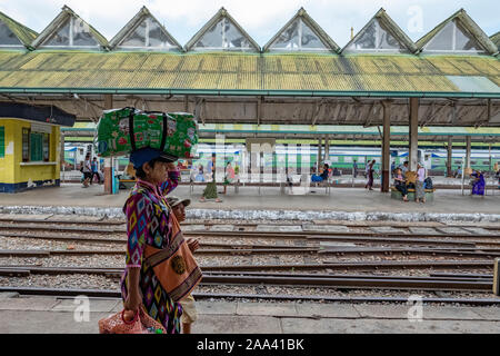 Der Hauptbahnhof von Yangon, Myanmar mit einem burmesischen Frau, die ein Bündel auf dem Kopf, als sie Spaziergänge entlang der Bahngleise mit ihrem Sohn Stockfoto