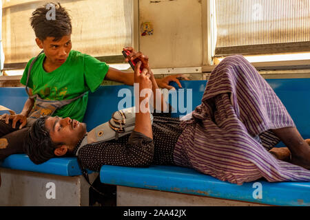 Zwei Jungen burmesischen Anbieter machen Sie eine Pause und einem Handy prüfen, während auf einem lokalen Zug auf dem Rundweg um Yangon, Myanmar (Birma) Stockfoto