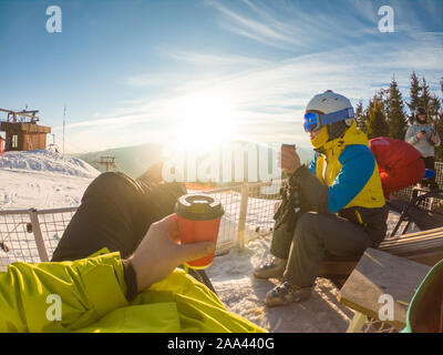Paar ruht auf der Oberseite des verschneiten Hügel trinken Kaffee aufwärmen. Snowboarden und Skifahren Stockfoto