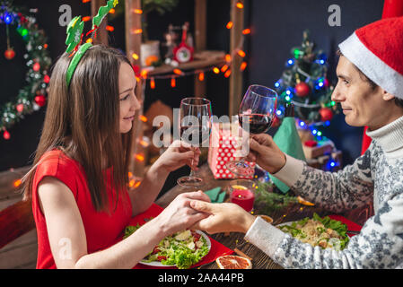 Junge schöne Paar Mann und Frau verbringen einen festlichen Abend speisen und trinken Wein aus Gläsern in die Weihnachtsdekorationen an Silvester Stockfoto