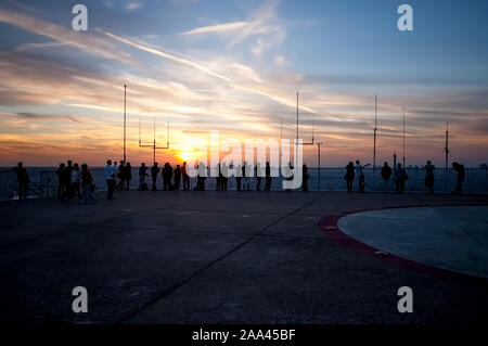 Eine Menge Leute auf einem Pariser Dach, die die Sonne über die Stadt hinuntergehen sehen Stockfoto