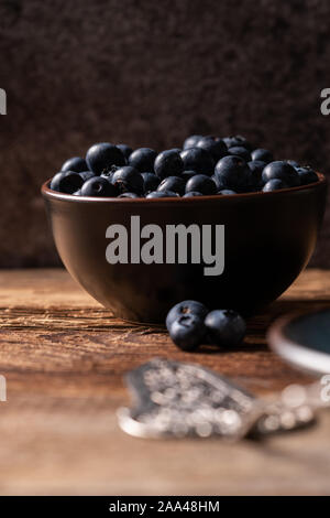 Frische reife Heidelbeeren in braun Keramik Schüssel auf Holztisch mit dunklem Hintergrund, Zutaten für gesunde Ernährung lifestyle Konzept, dunkel und Moody