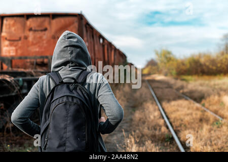 Obdachlose Frau mit Rucksack Entfliehen, Rückansicht der weiblichen Fuß unter verlassenen Waggons und veraltete Eisenbahn Stockfoto