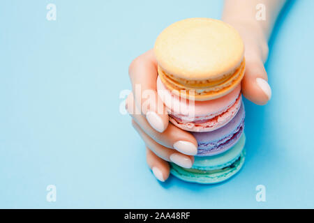 Schönheit hand Mädchen mit trendigen Maniküre unter Farbe makronen auf blauem Hintergrund. Stockfoto