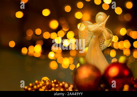 Traditionelle Handarbeit Stroh Puppe mit Weihnachten Ornamente auf einem verschwommenen Hintergrund mit Beleuchtung. Dramatische Weihnachten Landschaft mit getrocknetem Stroh Engel, Stockfoto
