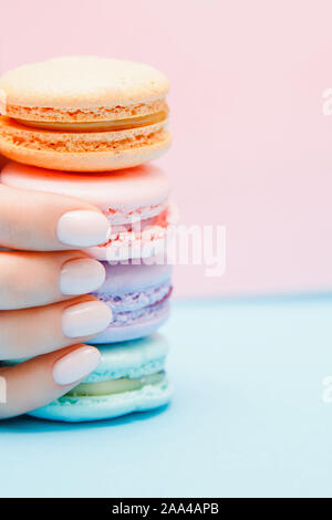 Schönheit hand Mädchen mit trendigen Maniküre unter Farbe makronen auf blauem Hintergrund. Stockfoto