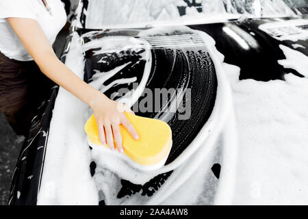 Hintergrund Hand halten Schwamm über schwarzen Auto waschen weißer Schaum. Stockfoto