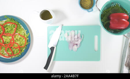 Zwiebel auf einem Schneidebrett, Nahaufnahme, Ansicht von oben. Salat auf einen Teller, auf weißem Hintergrund schliessen. Frische organische Römersalat, rot Pep Stockfoto