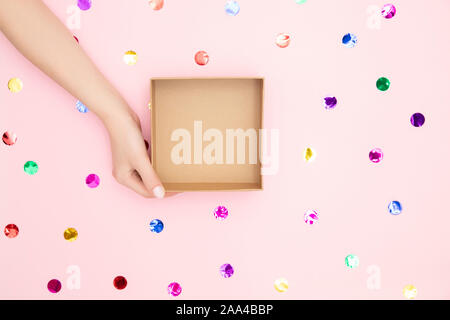 Schöne weibliche Hände halten ein leeres Profil Geschenkbox auf rosa Konfetti Hintergrund, Platz für Text. Stockfoto