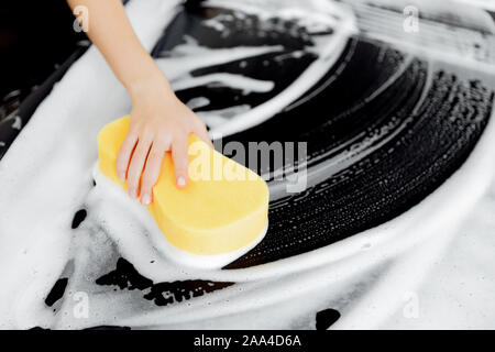 Hintergrund Hand halten Schwamm über schwarzen Auto waschen weißer Schaum. Stockfoto