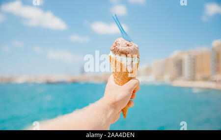 Mann hält Eis in Kegel mit Löffel gegen blaue Meer. Entspannung Konzept. Stockfoto