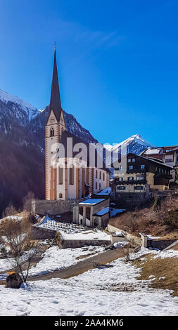 Kleine Kirche in Heiligenblut, Österreich, im Tal zwischen hohen Alpen. Masse s mit Schnee bedeckt. Einige Häuser rund um die Kirche Schöne f Stockfoto