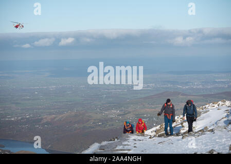 Snowdon Gipfels, Gwynedd, Wales, UK. 10. November 2019. Eine HM Küstenwache Rettungshubschrauber Patrouillen der Himmel über einem schneebedeckten Snowdon in Wales. Stockfoto