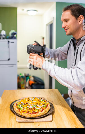 Mann, Fotograf, oben flach Bild von Hausgemachte warme Pizza mit Tomatensauce und Toppings orange vegan Cheddar Käse auf dem Küchentisch Stockfoto