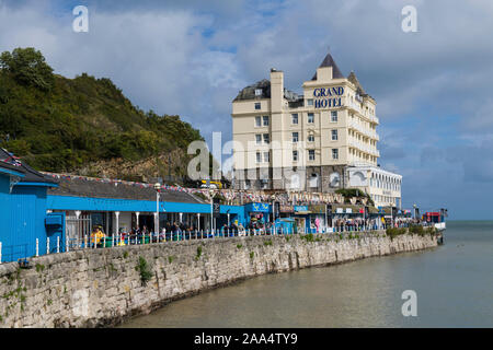 Das Grand Hotel an der Küste von Llandudno in Nordwales näherte sich über den Gehweg mit seinen Verkaufshütten und der steinernen Meeresmauer. Stockfoto