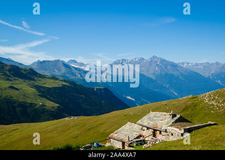 Alpine Landschaft im Sommer. Traditionelles Bauernhaus in einem alten Gebäude aus Stein hoch in den Alpen durch grüne Wiesen und Panoramablick umgeben Stockfoto