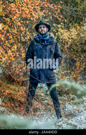 Bärtiger Mann lächelnd im Herbst und verschneiten Wald mit Hut Stockfoto