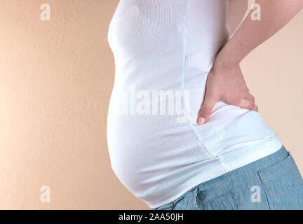 Zugeschnittenes Bild der schönen schwangere Frau ihren Bauch berühren und halten Sie eine Hand auf den Rücken. Stockfoto