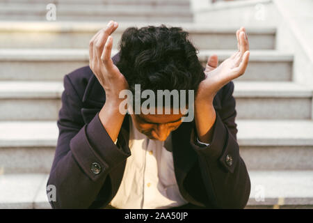 Junge indische Mann sitzt auf der Treppe und umklammerte seinen Kopf mit den Händen Stockfoto