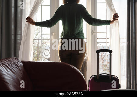 Eine Frau in Hosen stehen am Fenster im Wohnzimmer, Vorhänge Stockfoto