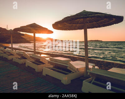 Sunsbeds und natürlichen Sonnenschirme am Strand mit Sonnenuntergang, Mykonos Griechenland Stockfoto