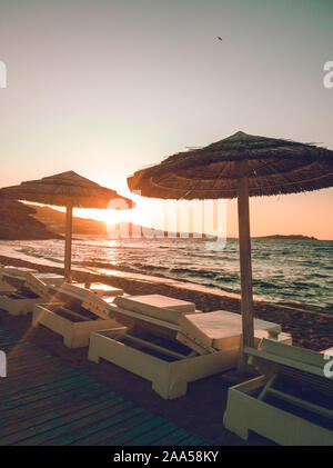 Sunsbeds und natürlichen Sonnenschirme am Strand mit Sonnenuntergang, Mykonos Griechenland Stockfoto